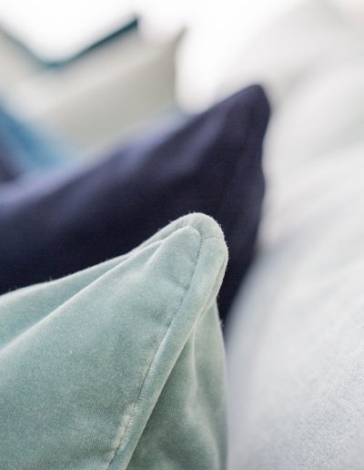 Close-up of velvet scatter cushions in shades of navy, teal and sage on a pale blue sofa.