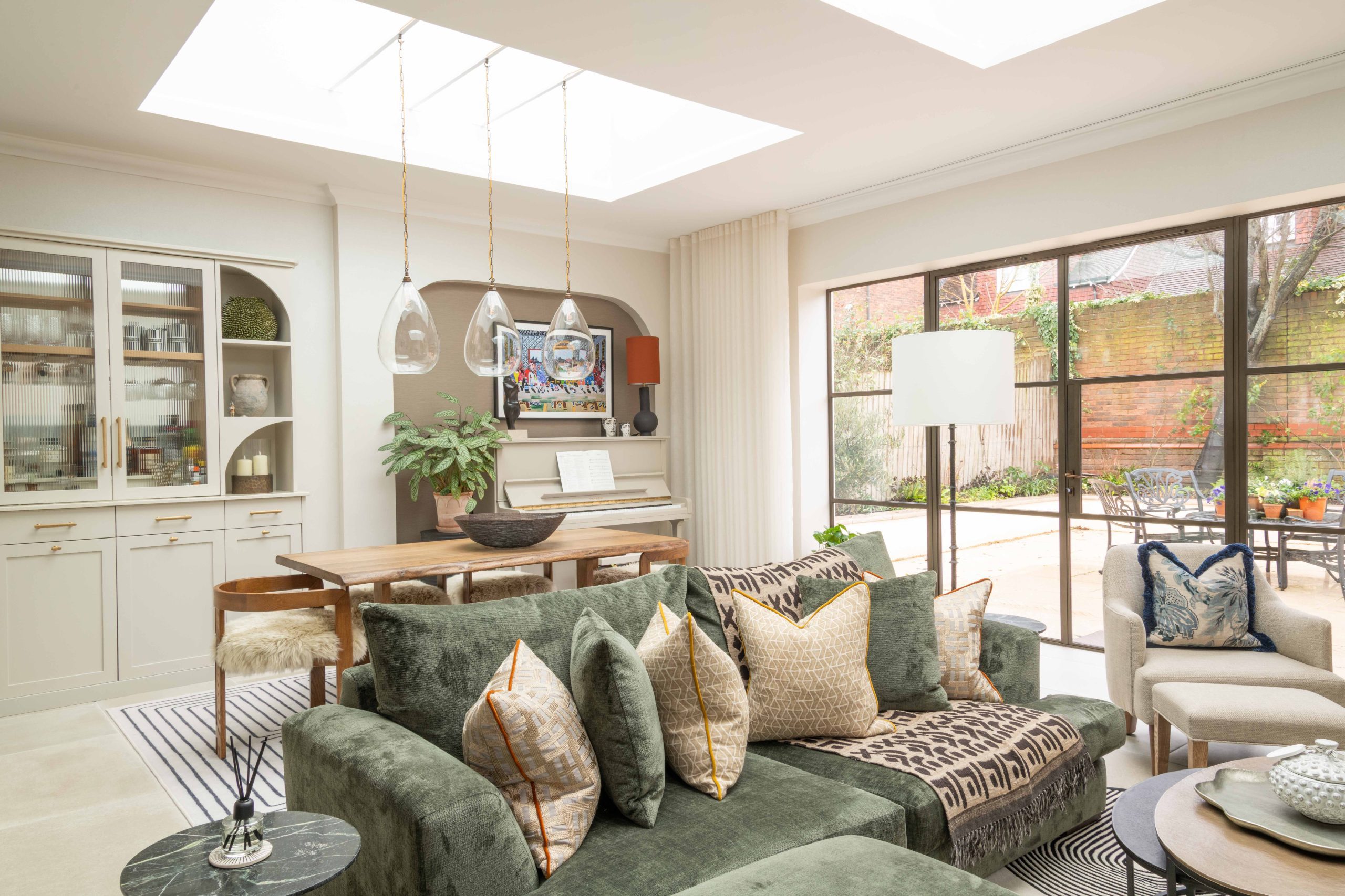 Orangery Extension in Over, Gloucester Contemporary orangery extension in Over, Gloucester with green velvet sofa, oak dining table, bespoke cabinetry and skylight bringing natural light into the open-plan space.