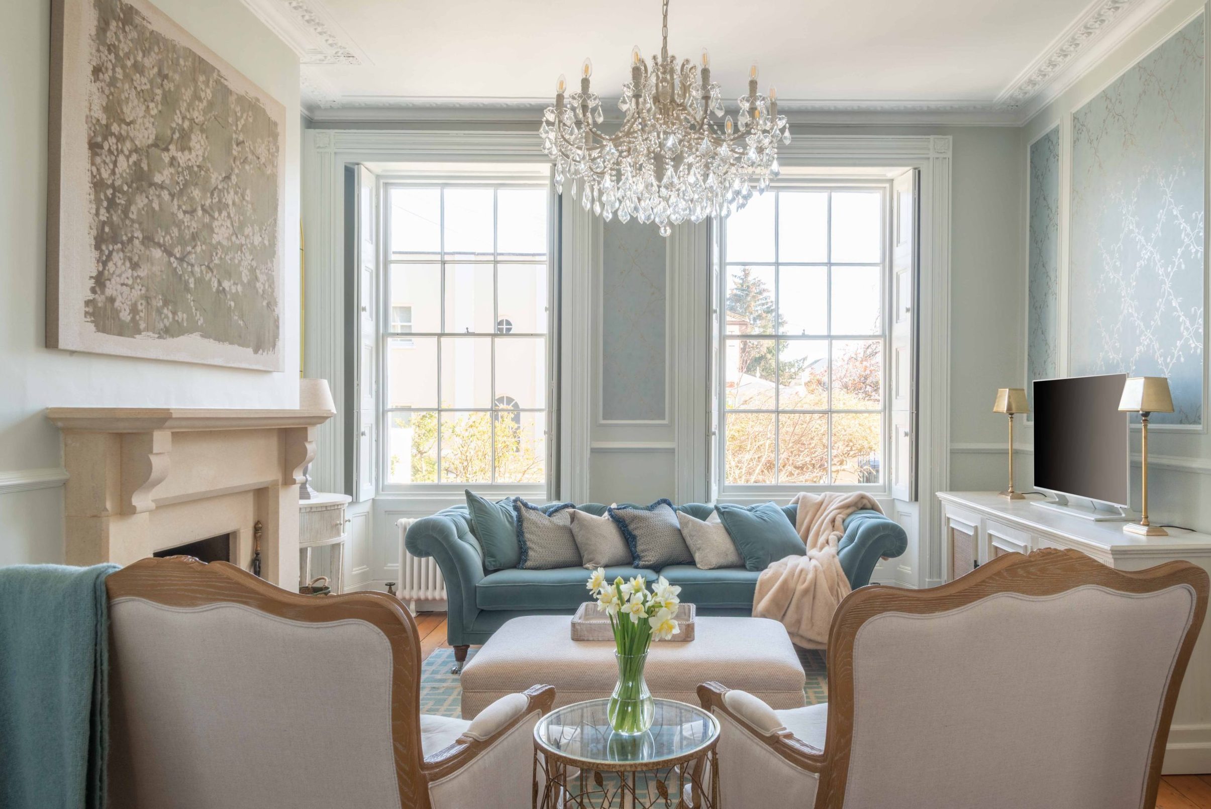 Finished living room interior design in Cheltenham Elegant living room with chandelier, blue sofa and large sash windows in a Cheltenham home.