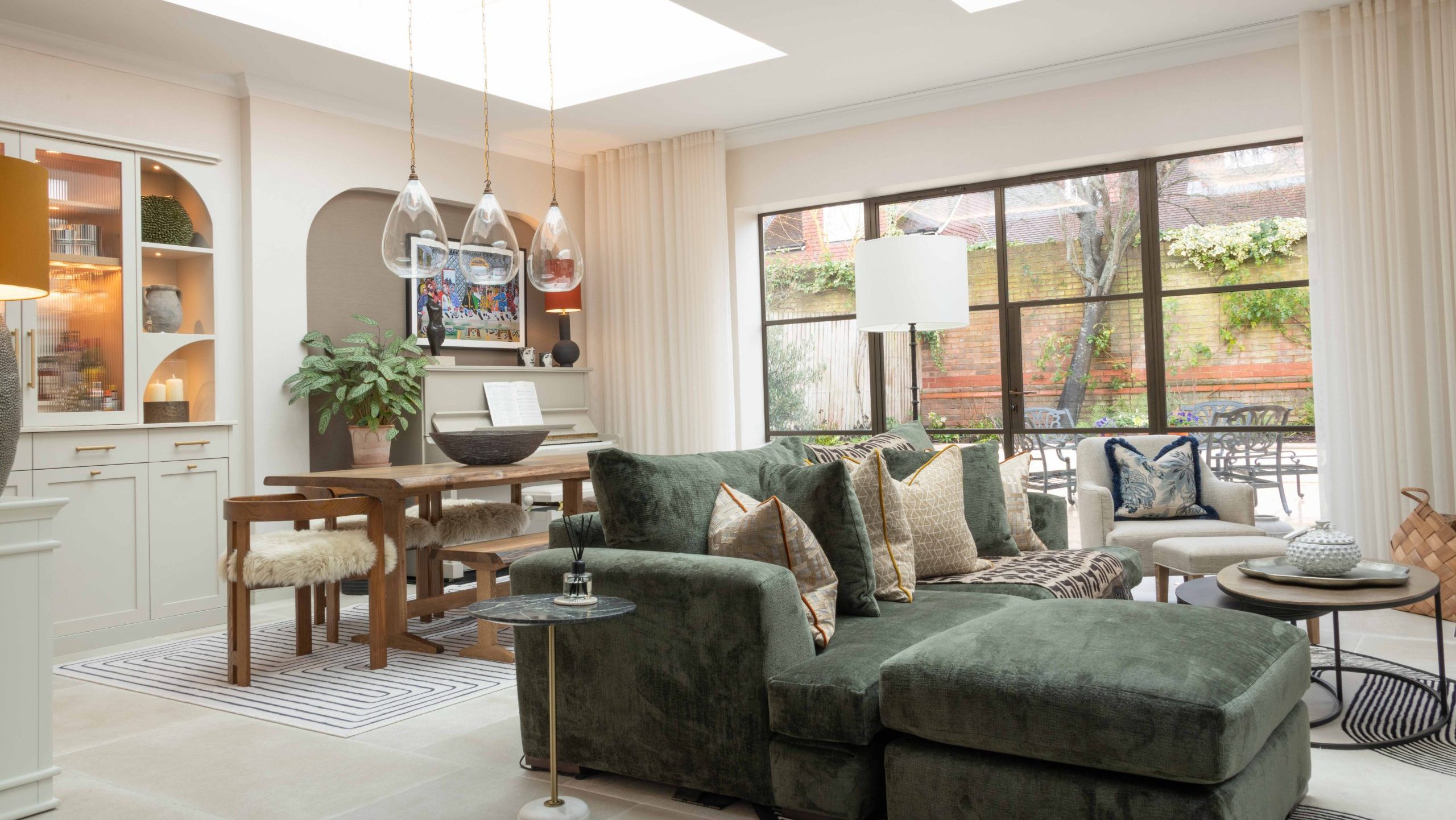 Orangery Extension in the Cotswolds Open-plan orangery living and dining space with green velvet sofa, timber dining table and large skylights