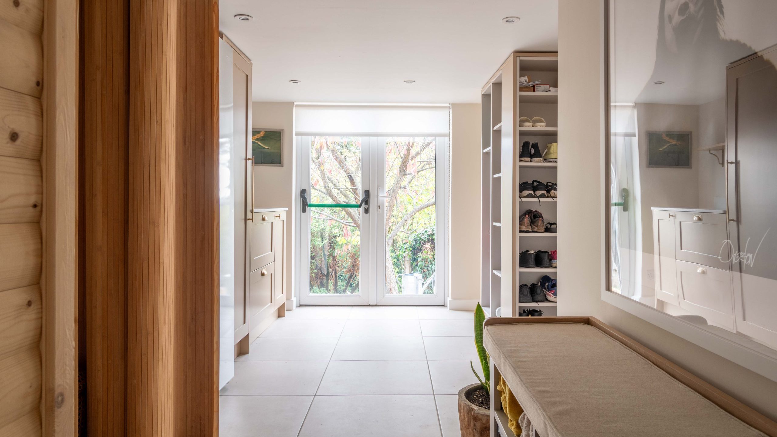After - boot room with bespoke shaker cabinetry, full-height shoe shelving, upholstered bench, curved bamboo sauna screen, large format floor tiles and garden beyond, designed by The House Ministry.