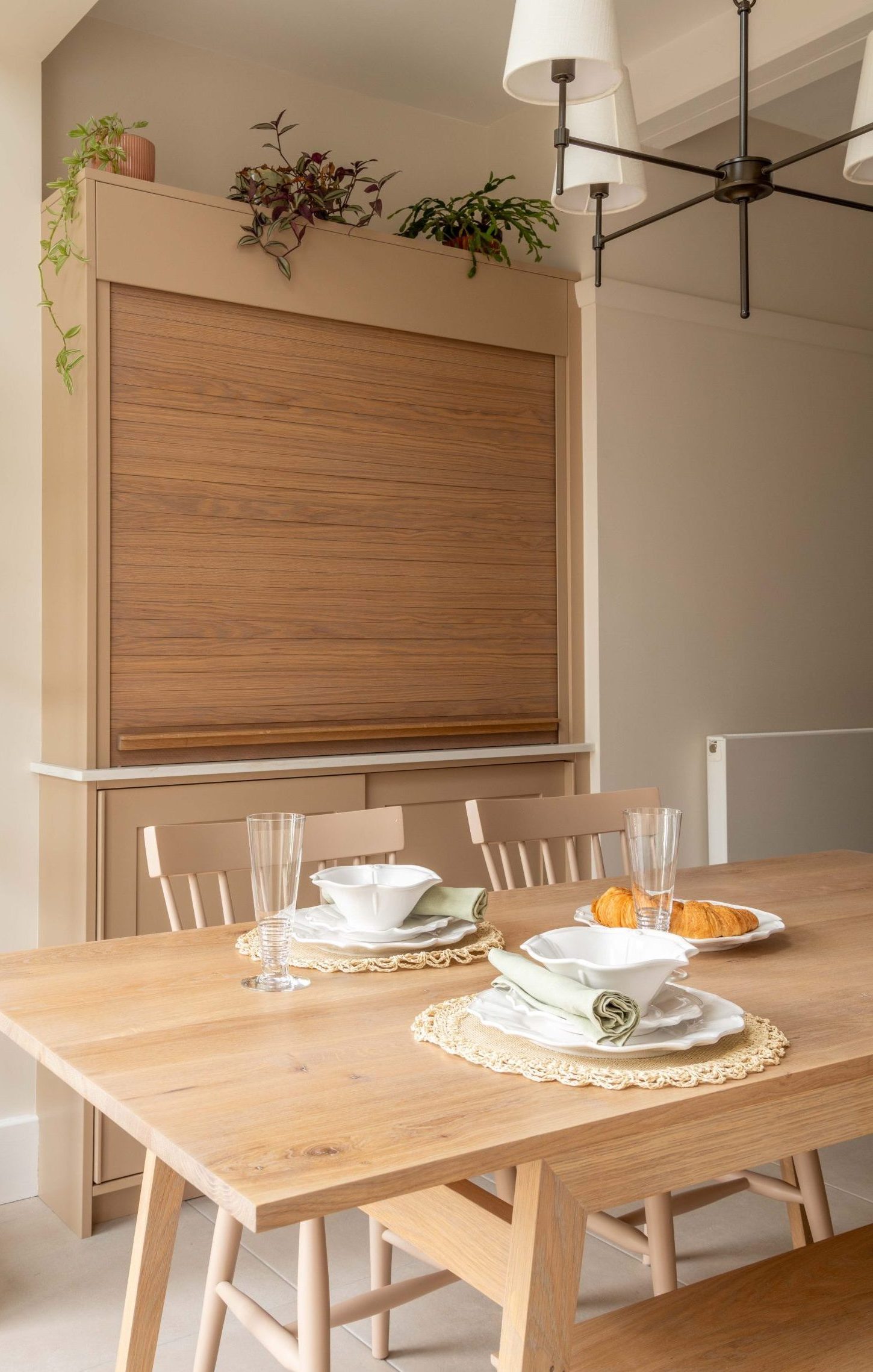 Bespoke concealed bar with oak tambour door closed, set within kitchen-diner alongside oak dining table and multi-arm pendant light, designed by The House Ministry.
