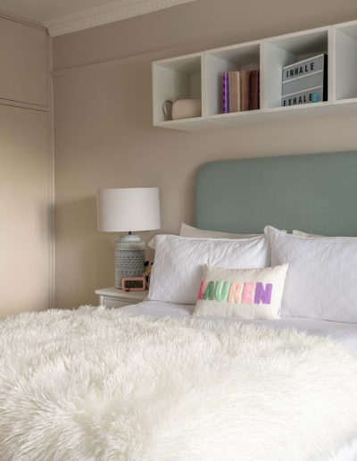 Tweenager's bedroom with duck egg blue upholstered headboard, wall-mounted display shelving, existing wardrobes painted to match the scheme and neutral bedside tables, designed by The House Ministry.