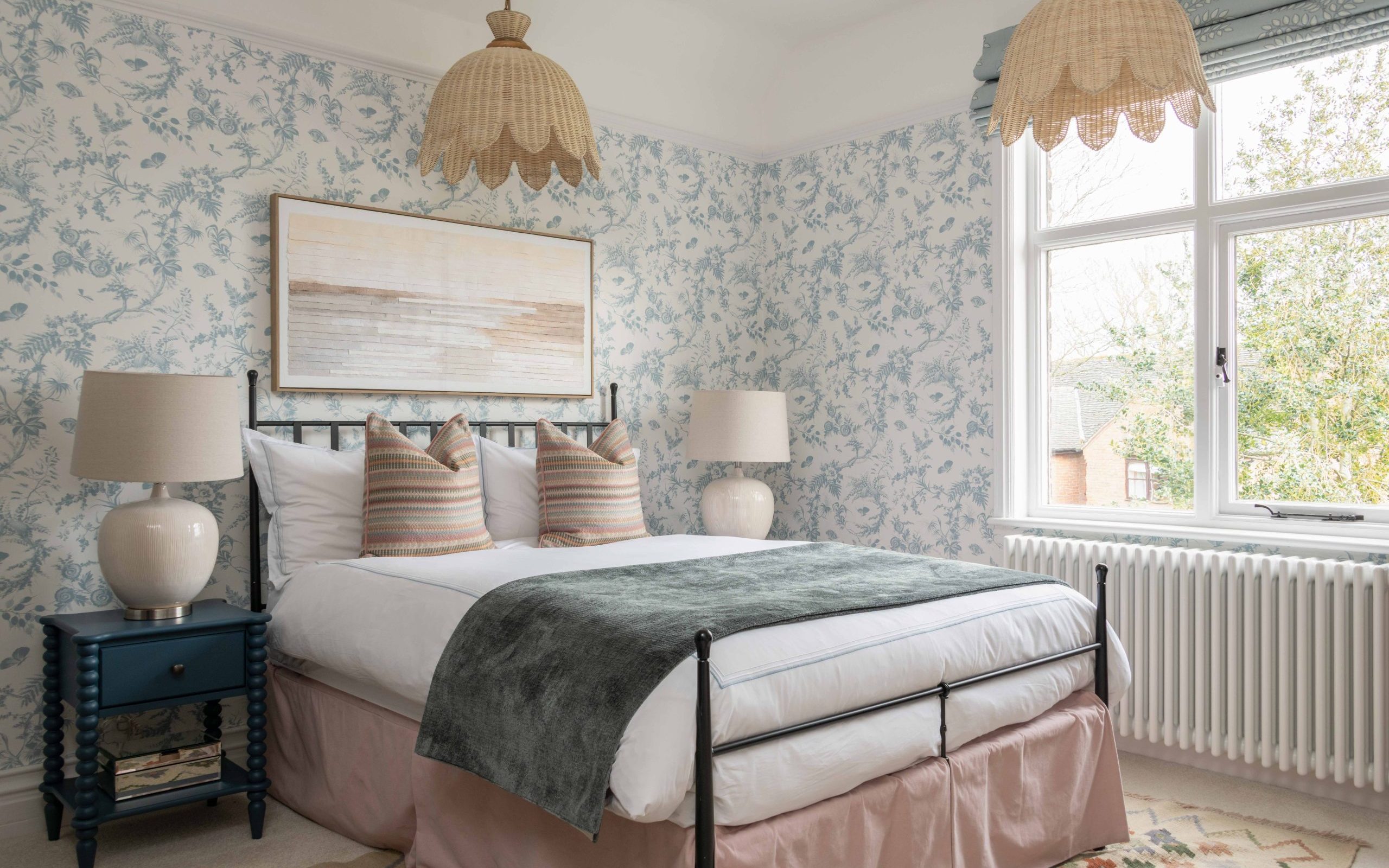 Edwardian Family Home Bedroom Redesign | The House Ministry Bedroom in an Edwardian family home - blue and white floral wallpaper, black iron bed frame, wicker scalloped pendant lights, navy bobbin bedside table and garden view, designed by The House Ministry.