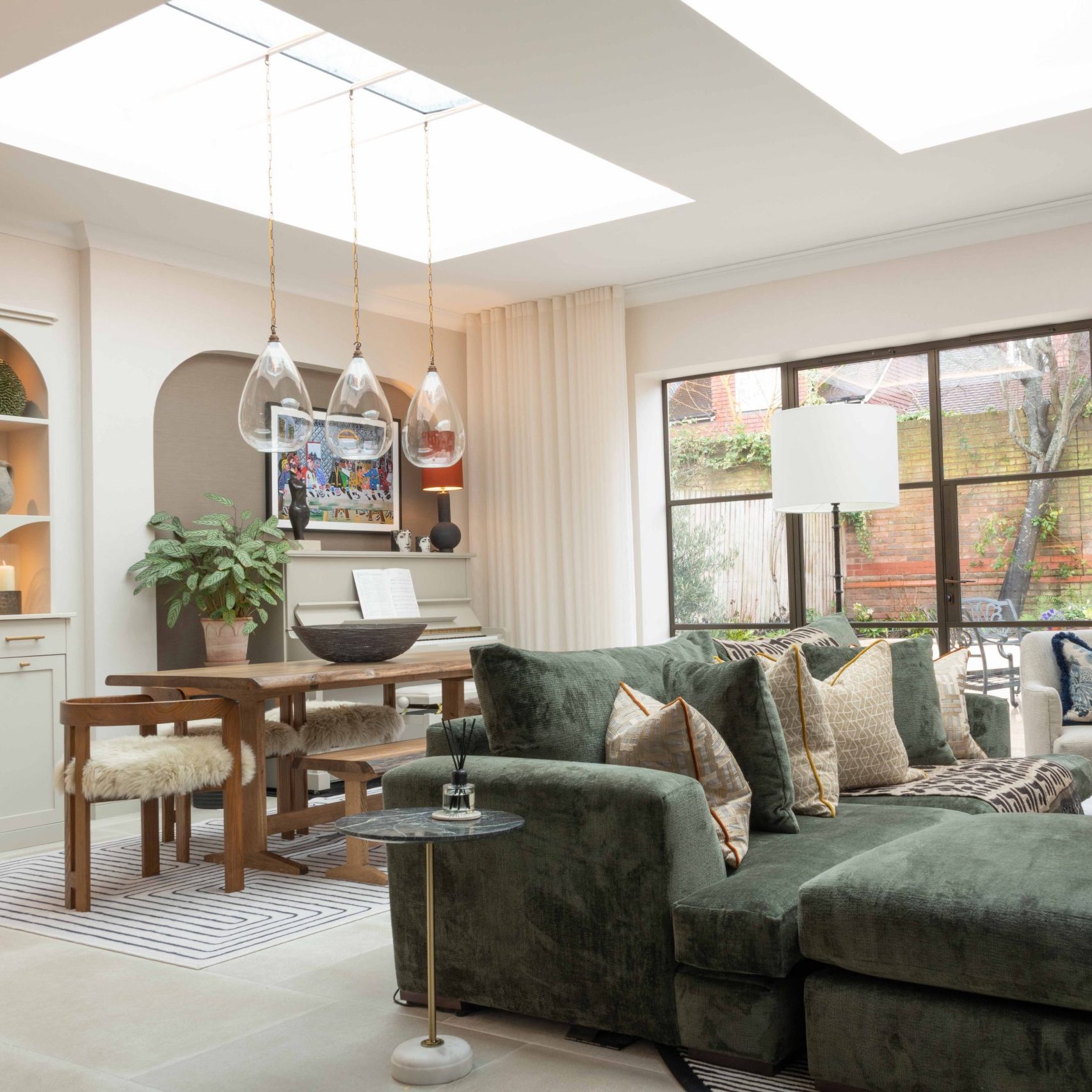 Orangery Extension in the Cotswolds Open-plan orangery living and dining space with green velvet sofa, timber dining table and large skylights