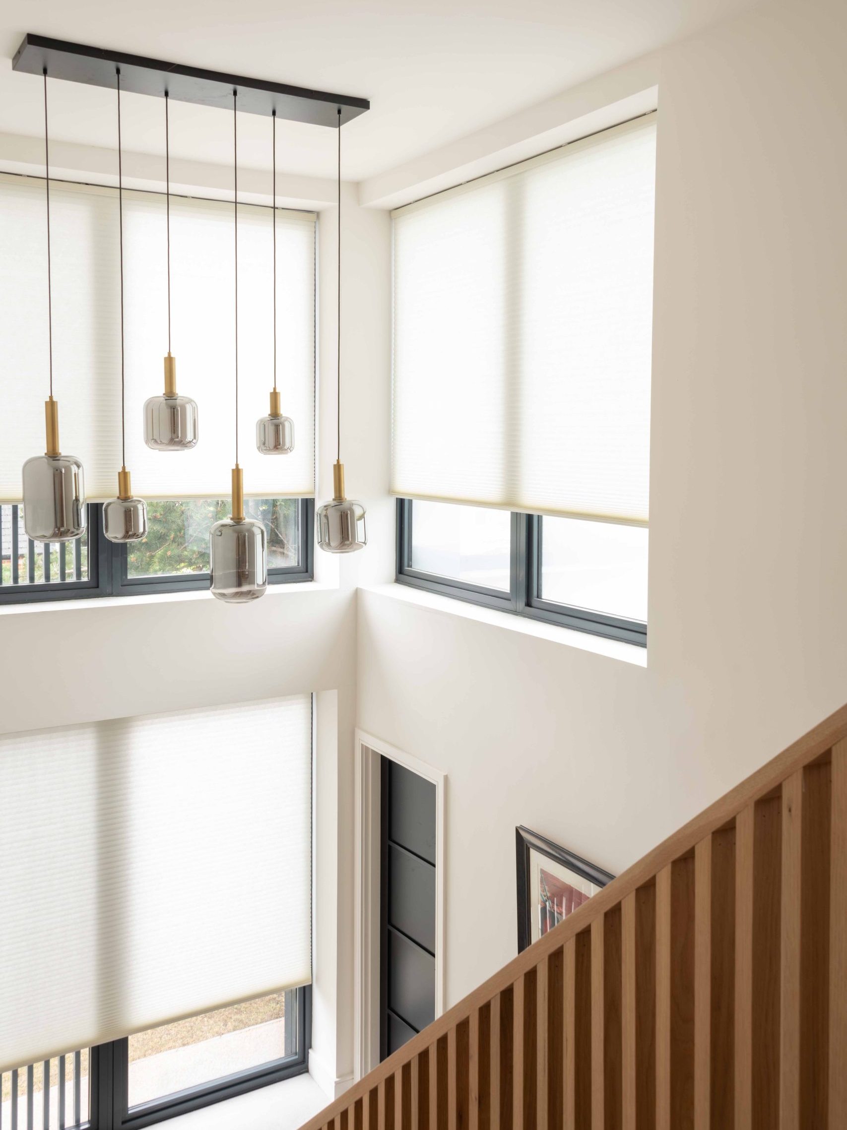 Double-Height Stairwell with Pendant Lighting | The House Ministry Double-height stairwell with cluster of smoked glass pendant lights, roller blinds and oak slatted balustrade