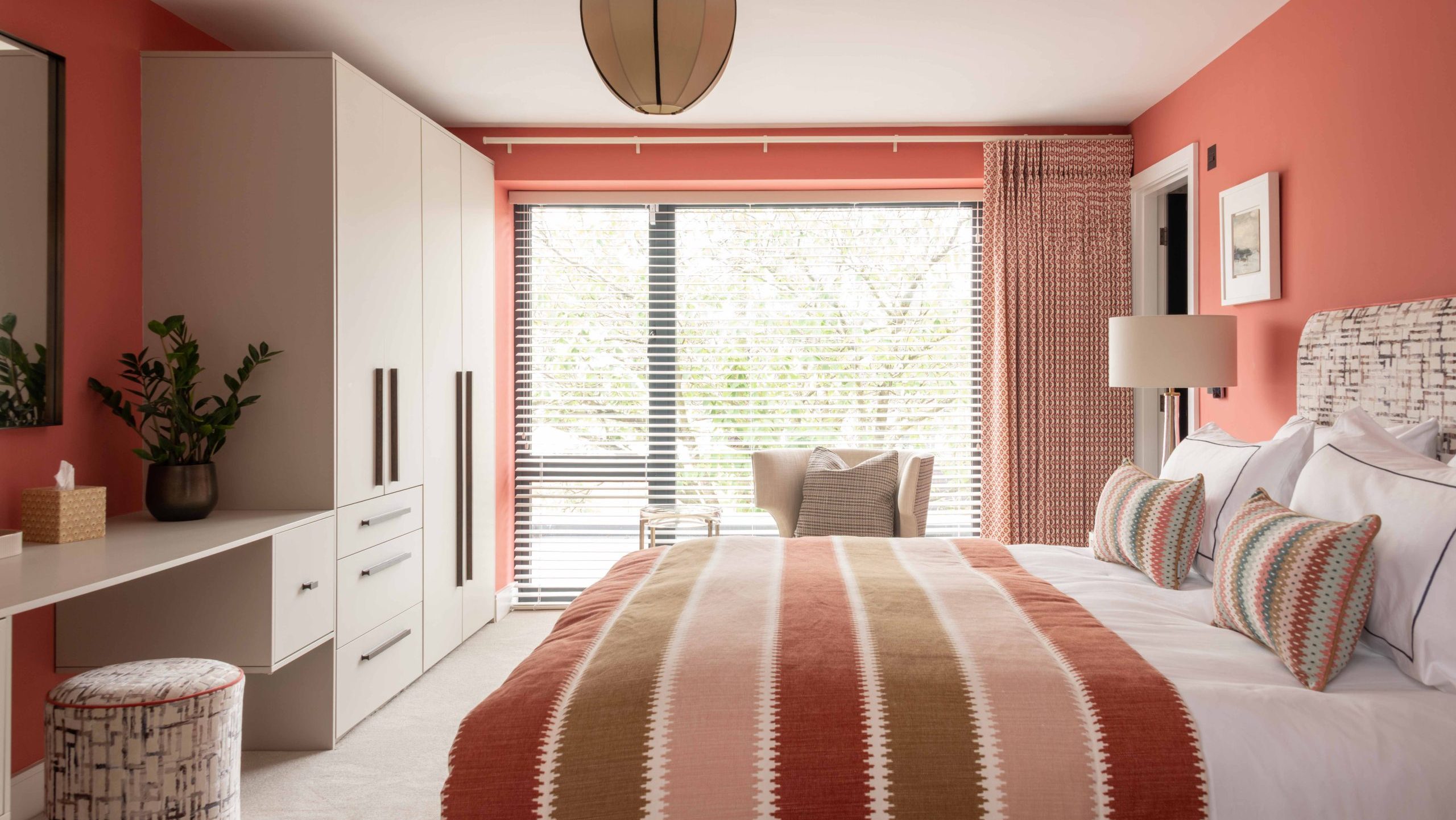 After - Guest Bedroom Interior After Renovation | The House Ministry After - Finished bedroom with coral walls, patterned curtains, striped bedspread and upholstered headboard