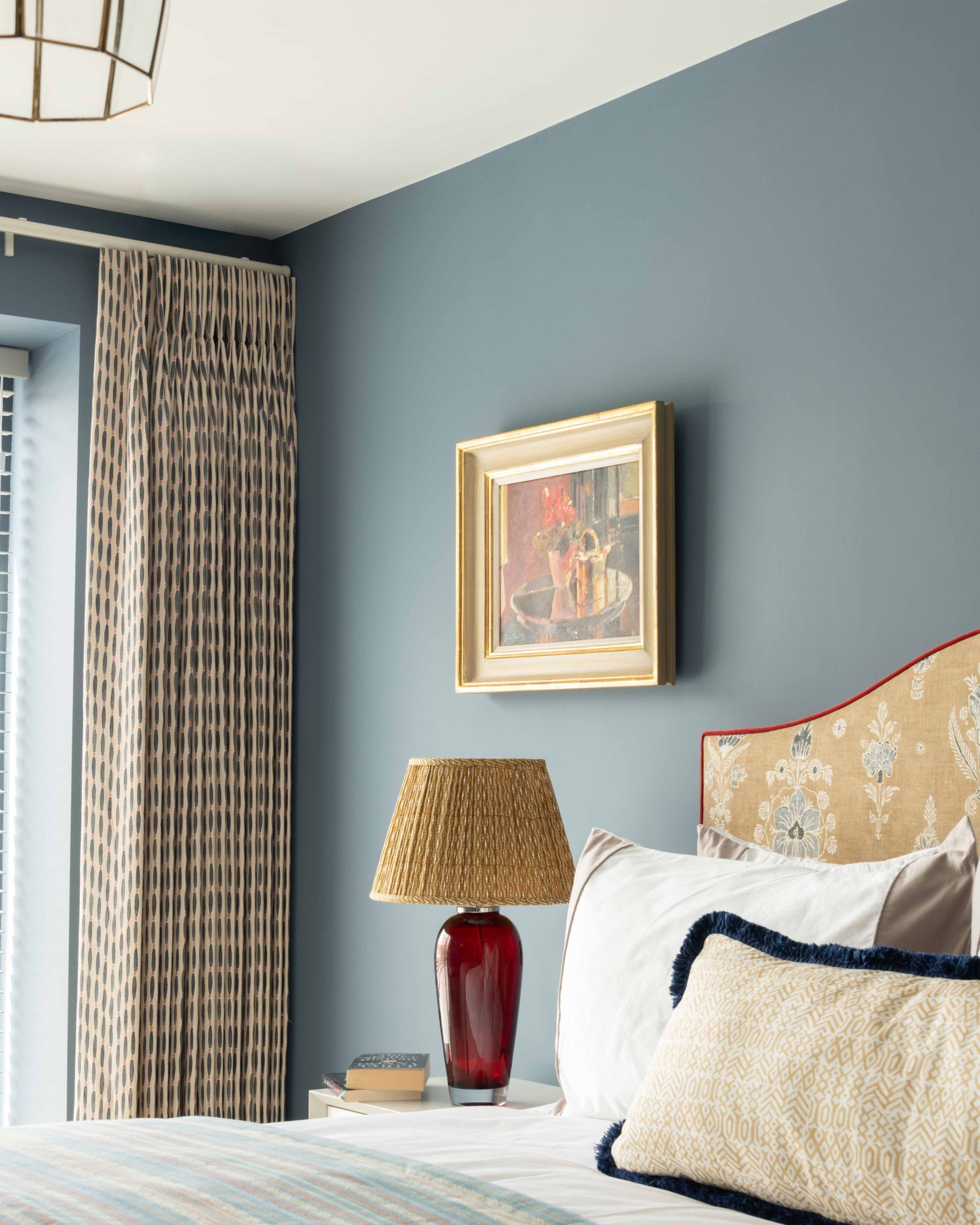 After - Guest Bedroom After Interior Renovation | The House Ministry After - Guest bedroom with blue walls, patterned curtains, striped bedspread and a red glass table lamp