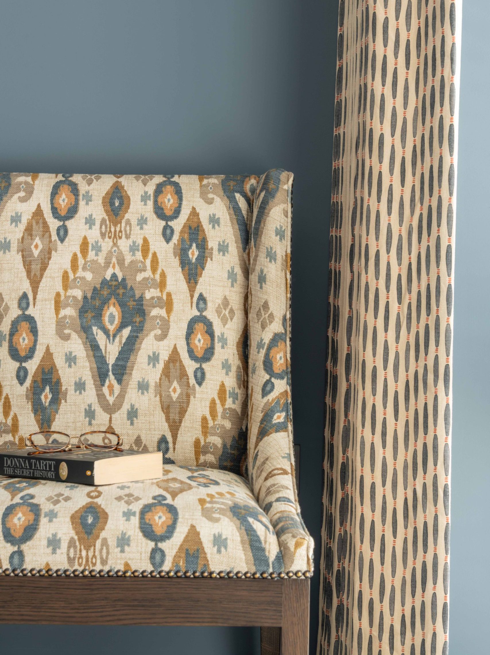 Ikat Wingback Chair and Curtain Detail | The House Ministry Ikat-patterned wingback chair beside a geometric patterned curtain, with glasses and a book resting on the seat